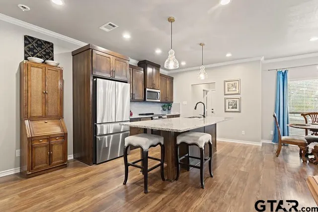 a kitchen with granite countertop a refrigerator a sink dishwasher a stove a dining table and chairs with wooden floor