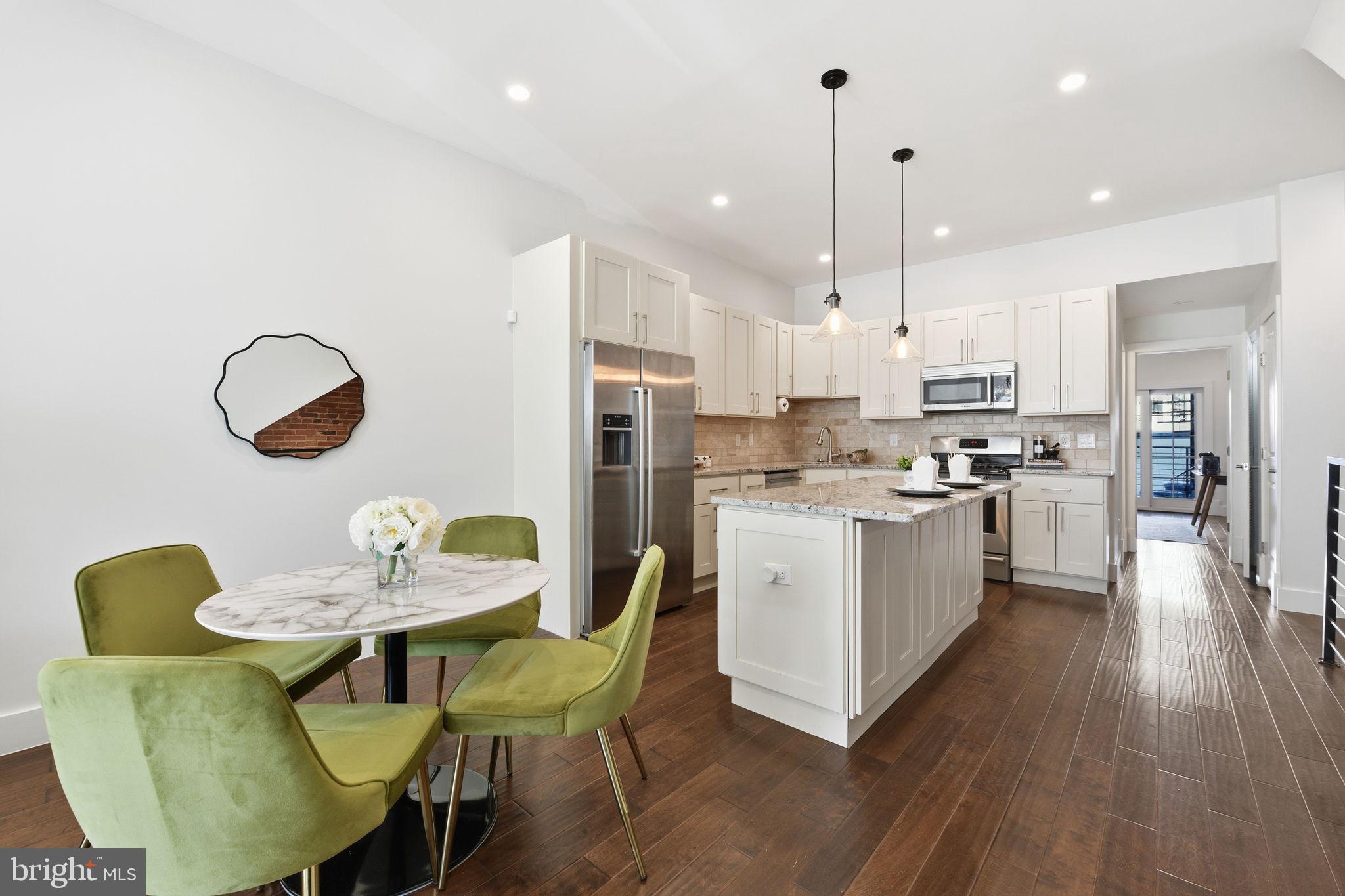 26 Q Street Northeast, Unit 1 Washington, DC 20002 - Photo 5 of 36 a kitchen with stainless steel appliances kitchen island granite countertop a dining table chairs and a refrigerator