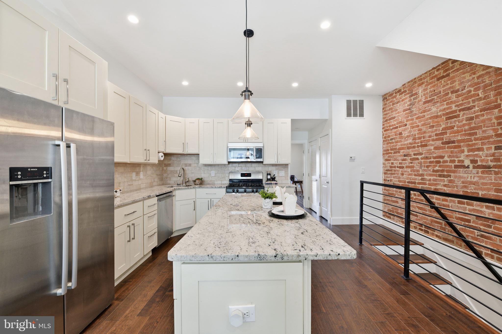 26 Q Street Northeast, Unit 1 Washington, DC 20002 - Photo 9 of 36 a kitchen with granite countertop kitchen island stainless steel appliances a refrigerator a sink and wooden floor