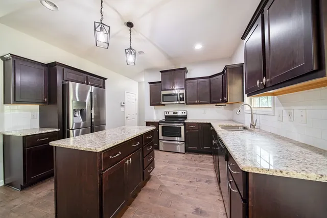 a kitchen with kitchen island granite countertop stainless steel appliances cabinets a sink and a counter top space
