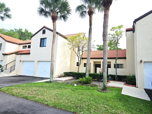 a view of a white house next to a yard with palm trees