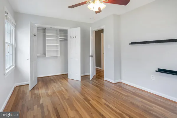 an empty room with wooden floor chandelier fan and windows