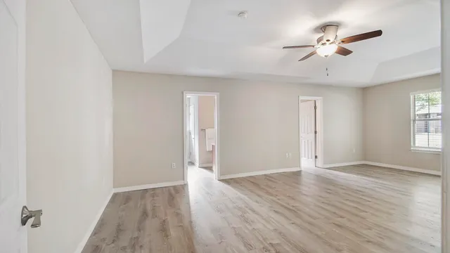 an empty room with wooden floor ceiling fan and windows