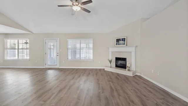 an empty room with wooden floor fireplace and windows