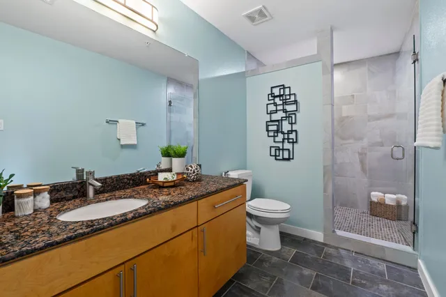 a bathroom with a granite countertop sink a toilet a mirror and shower