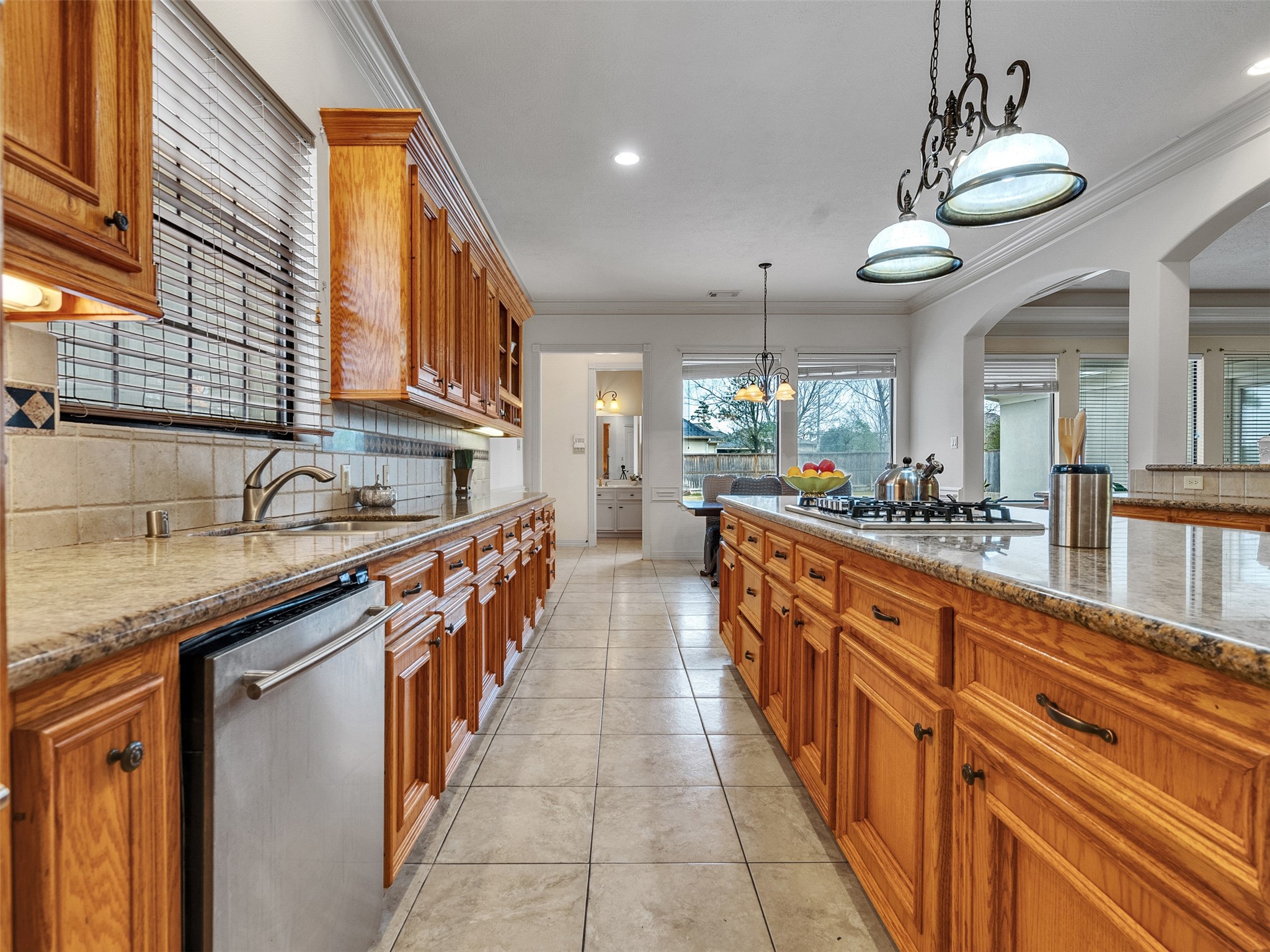 6914 Sandwedge Point Court Spring, TX 77389 - Photo 29 of 50 Spacious kitchen with ample natural light, featuring wooden cabinetry, granite countertops, and a central island with a built-in cooktop. The tiled floor and large windows enhance the open, inviting atmosphere.
