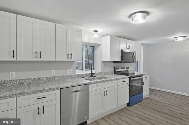 a kitchen with a sink dishwasher a stove and white cabinets with wooden floor