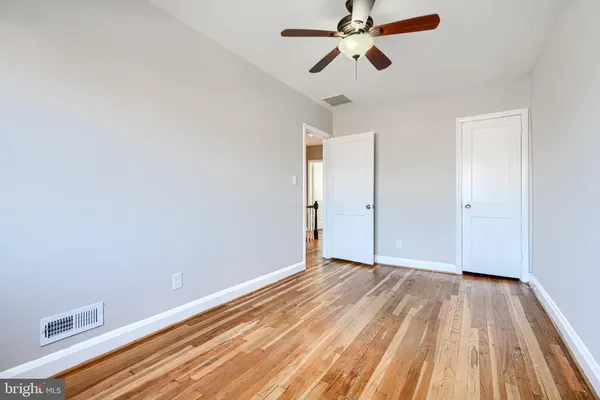 a view of an empty room with wooden floor and a ceiling fan