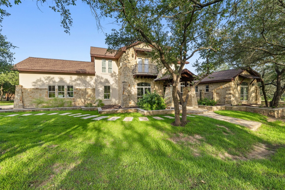 View of front of property with a balcony, a front yard, stucco siding, roof with shingles, and a patio