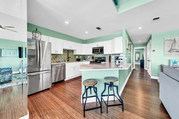 a kitchen with stainless steel appliances a refrigerator a stove top oven a sink dishwasher and white cabinets with wooden floor