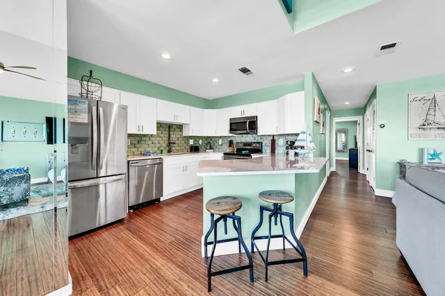 a kitchen with stainless steel appliances a refrigerator a stove top oven a sink dishwasher and white cabinets with wooden floor