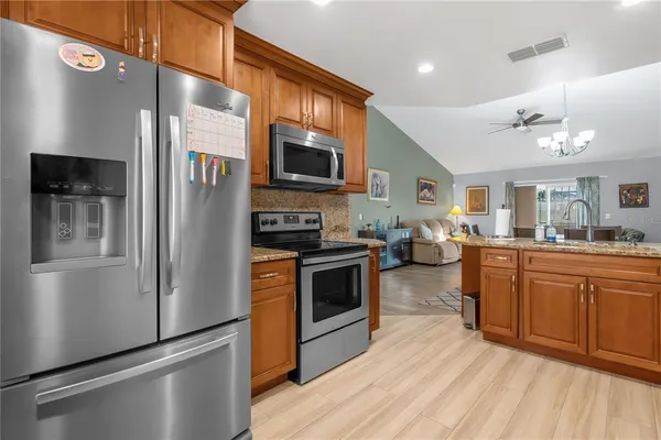 a kitchen with stainless steel appliances granite countertop a refrigerator a stove top oven a sink dishwasher and wooden cabinets with wooden floor
