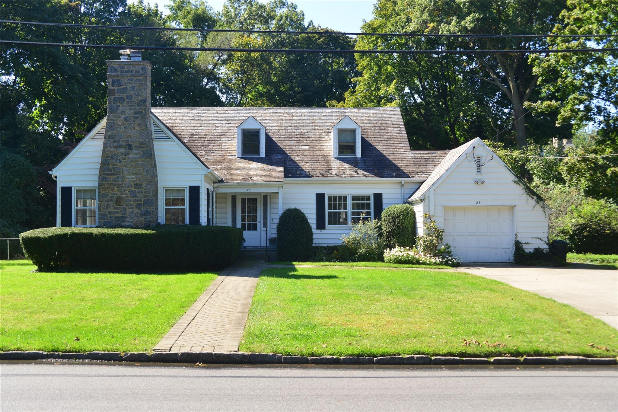 Cape cod-style house featuring a front lawn, driveway, a chimney, and an attached garage