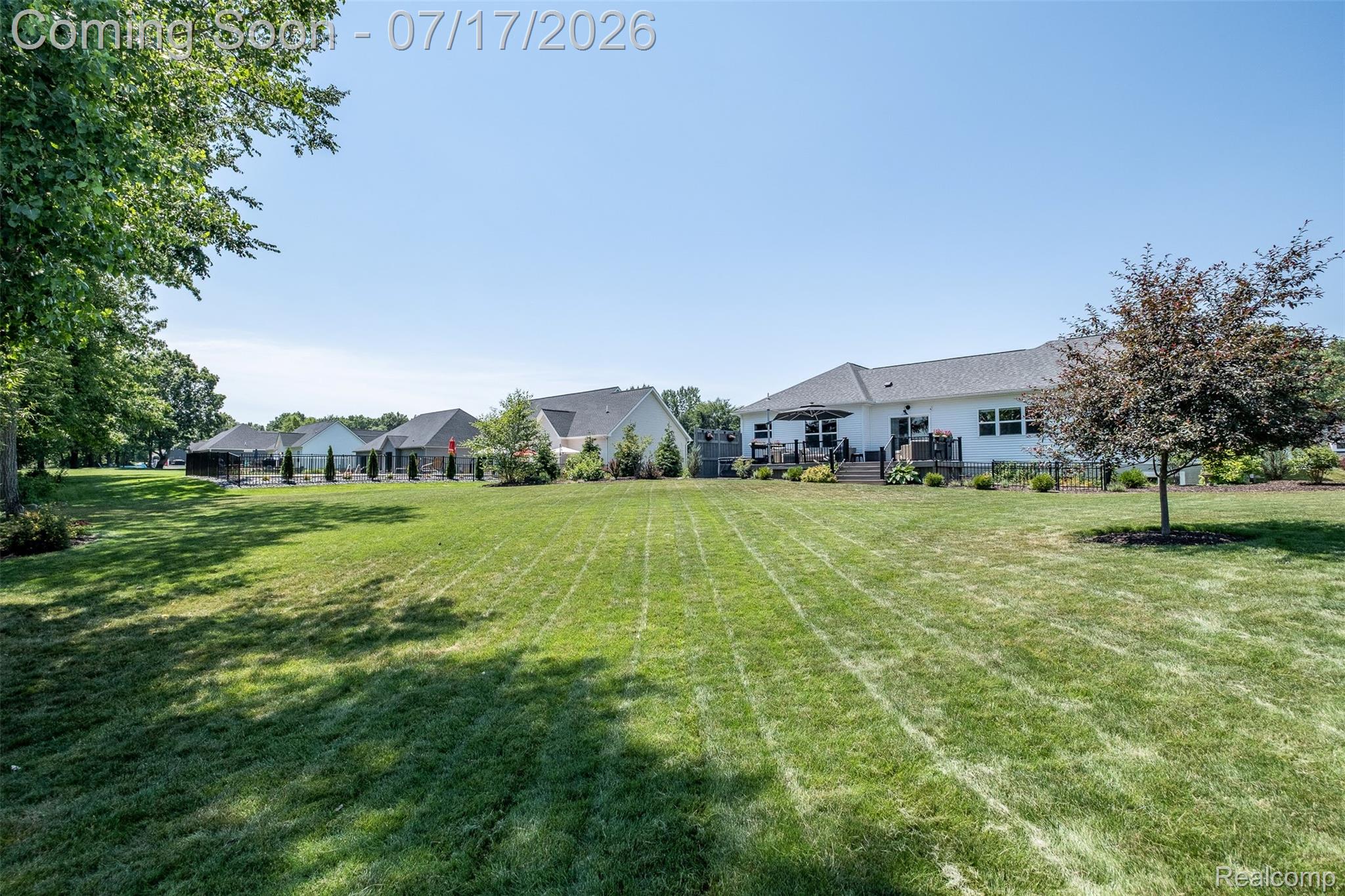 12349 Sugar Maple Drive Fenton, MI 48430 - Photo 56 of 67 Spacious green lawn extending towards a single-story white residence featuring a dark-colored deck and mature trees