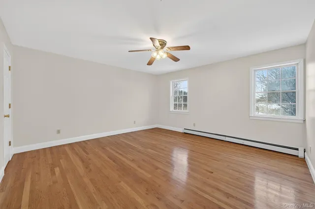 an empty room with wooden floor ceiling fan and windows