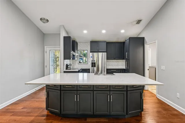 a room with kitchen island stainless steel appliances sink cabinets and wooden floor