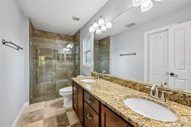 a bathroom with a granite countertop double vanity sink a mirror and a shower