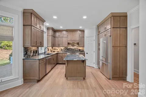 a kitchen with stainless steel appliances granite countertop a refrigerator a sink dishwasher a stove and a dining table with wooden floor