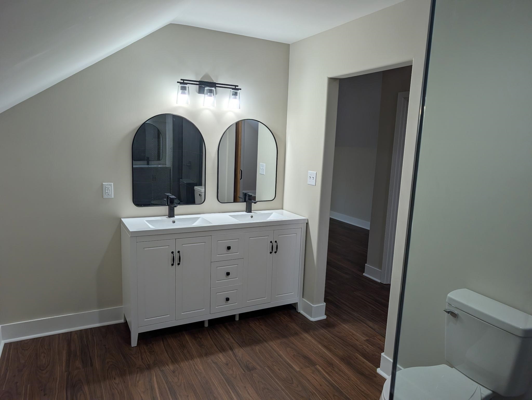 3540 Portersville Road Atoka, TN 38004 - Photo 30 of 37 Dual sink vanity with white cabinetry and matte black hardware, accented by two arched mirrors and a three-light fixture