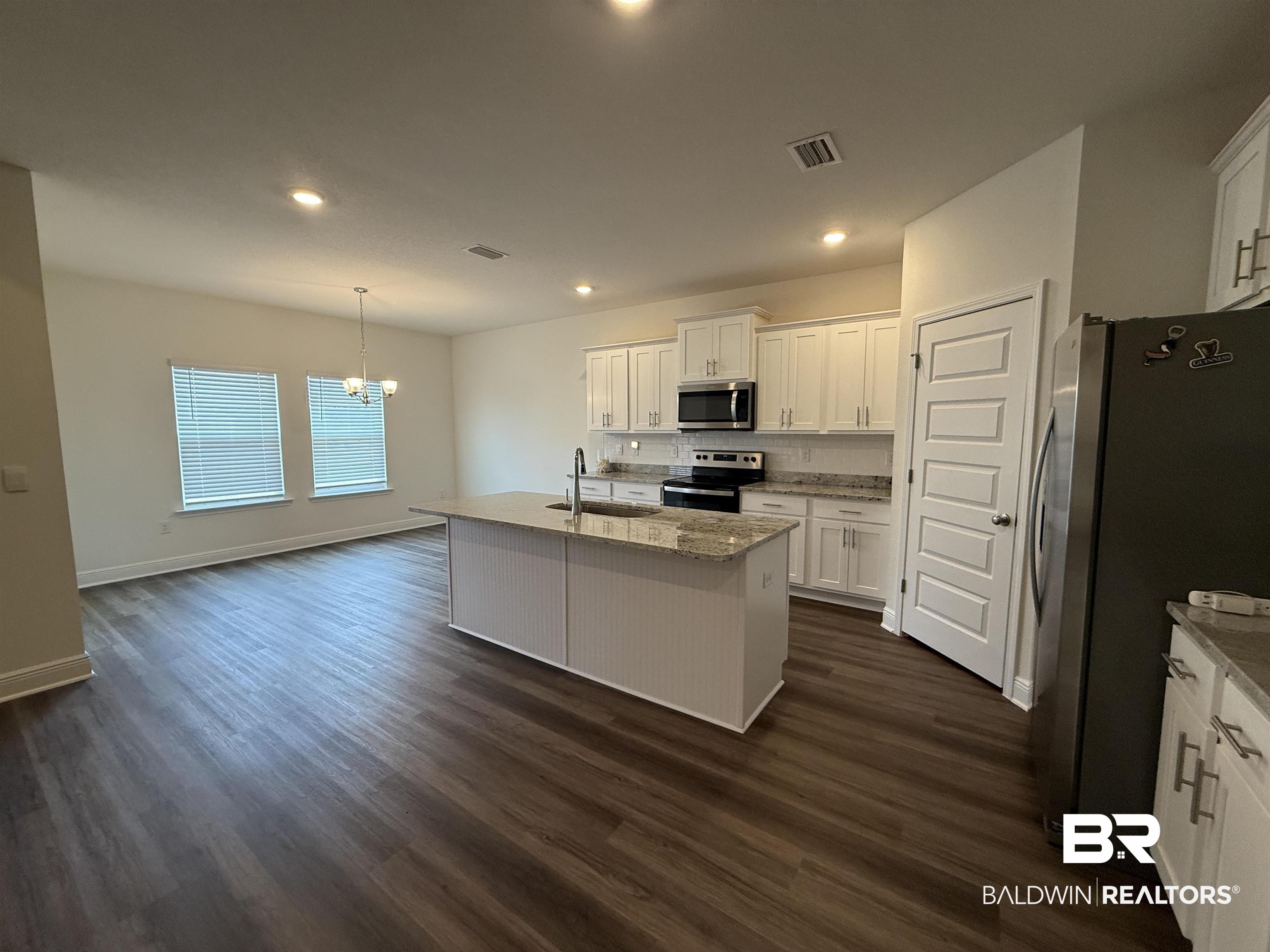 11442 Genuine Risk Circle Daphne, AL 36526 - Photo 4 of 21 Kitchen featuring stainless steel appliances, white cabinetry, light stone countertops, hanging lights, and a center island with sink