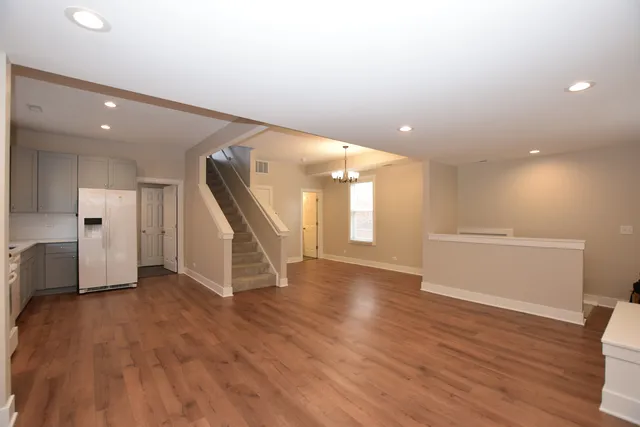 a view of an empty room with wooden floor and a kitchen