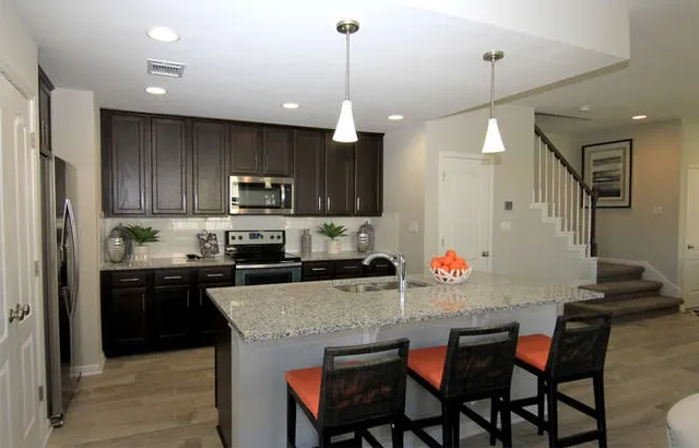 a kitchen with stainless steel appliances granite countertop a stove top oven a refrigerator a sink and chairs