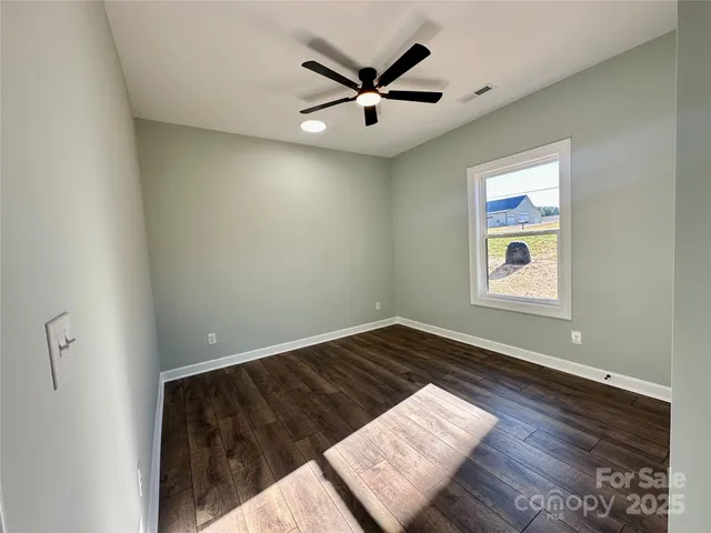a view of an empty room with wooden floor and a ceiling fan