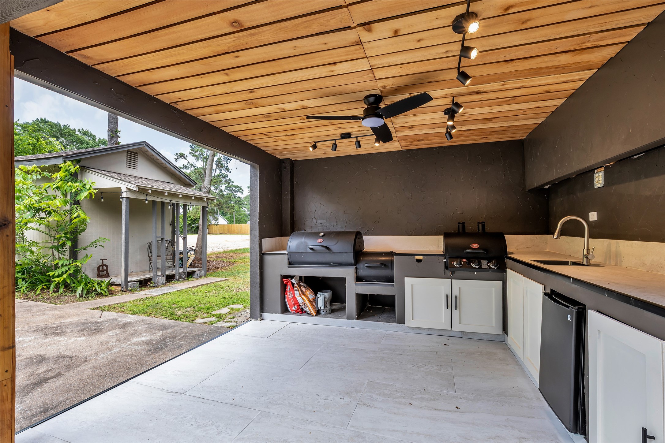 22502 Fields Lane Spring, TX 77389 - Photo 36 of 39 Modern outdoor kitchen with sleek cabinetry, a built-in grill, and a sink. The space is well-lit with track lighting and features a wood-paneled ceiling with a fan. Adjacent is a shed, shed offering extra storage or workspace.