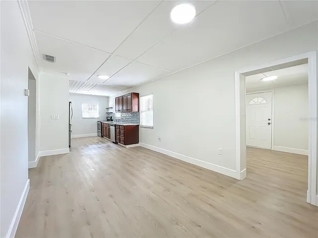 an empty room with wooden floor and kitchen