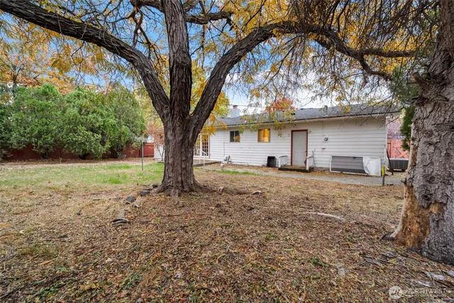 a backyard of a house with large trees and table and chairs