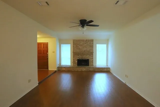 an empty room with wooden floor a fireplace and windows