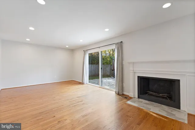 a view of an empty room with wooden floor and a kitchen