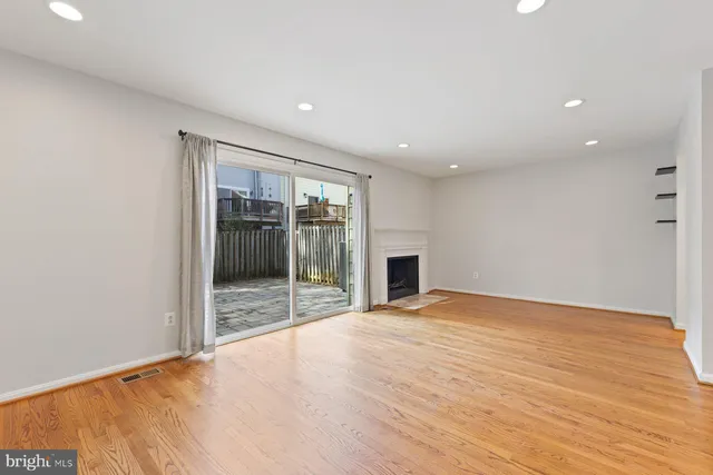 a view of an empty room with wooden floor and a kitchen