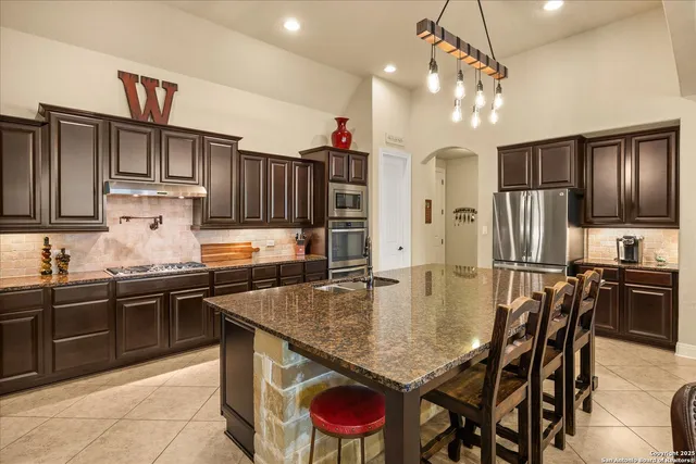 a kitchen with stainless steel appliances granite countertop a stove refrigerator a sink a dining table and chairs