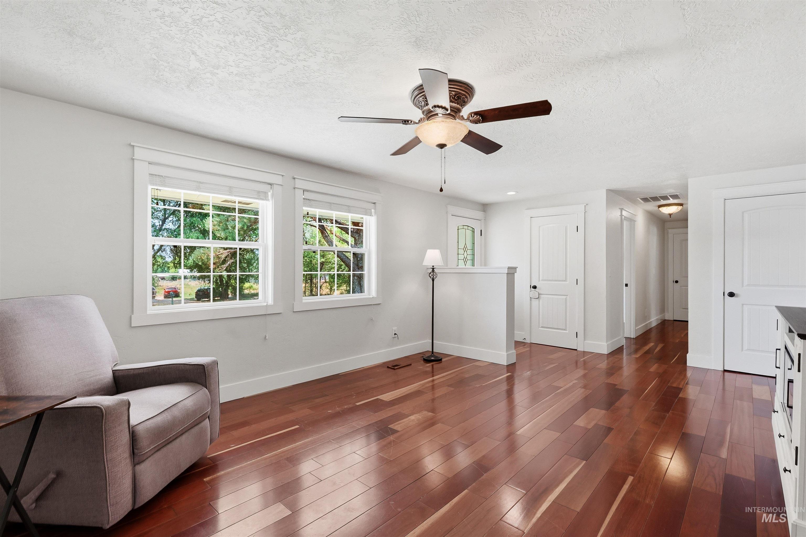 23650 Freezeout Road Caldwell, ID 83607 - Photo 6 of 42 Spacious living area featuring polished wood-finish flooring, a ceiling fan with integrated lighting, and two large multi-pane windows