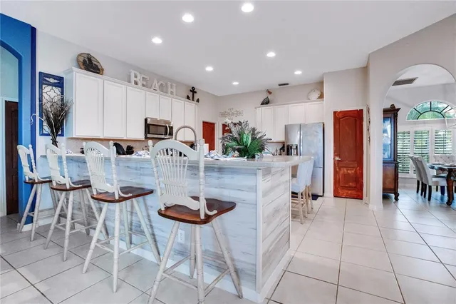 a kitchen with stainless steel appliances kitchen island granite countertop a refrigerator a stove a microwave oven with white cabinets and chairs