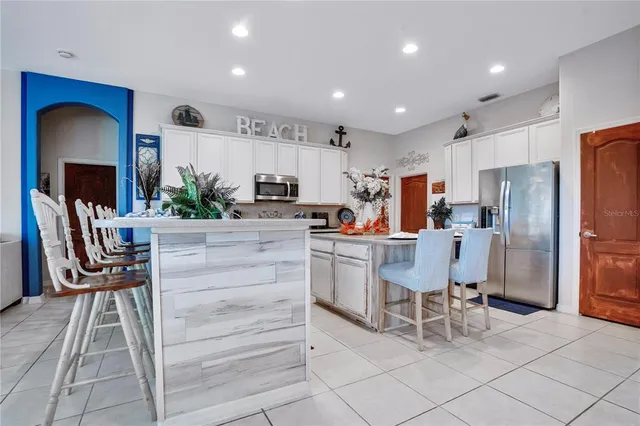 a kitchen with stainless steel appliances granite countertop a dining table chairs refrigerator and sink