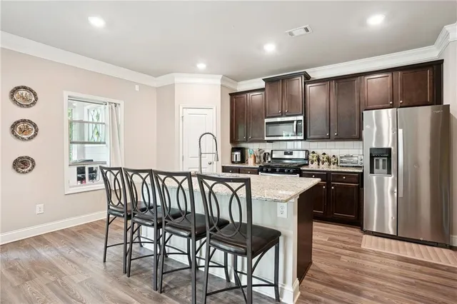 a kitchen with stainless steel appliances granite countertop a refrigerator a stove a sink a dining table and chairs with wooden floor