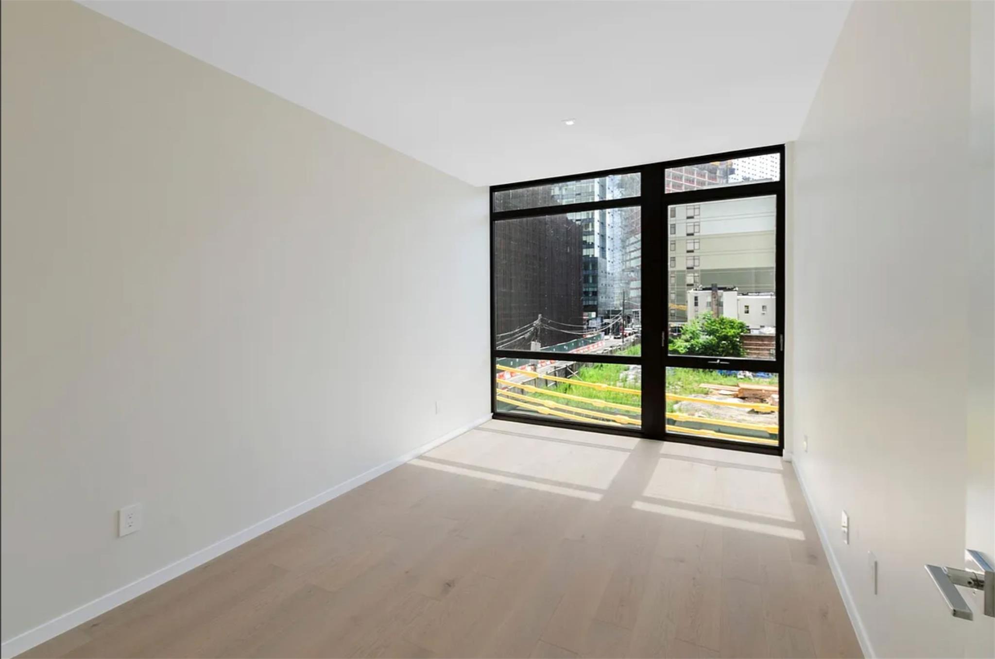 24-12 42nd Road, Unit 3E Queens, NY 11101 - Photo 4 of 13 Empty room featuring wood finished floors, a wall of windows, and a city view