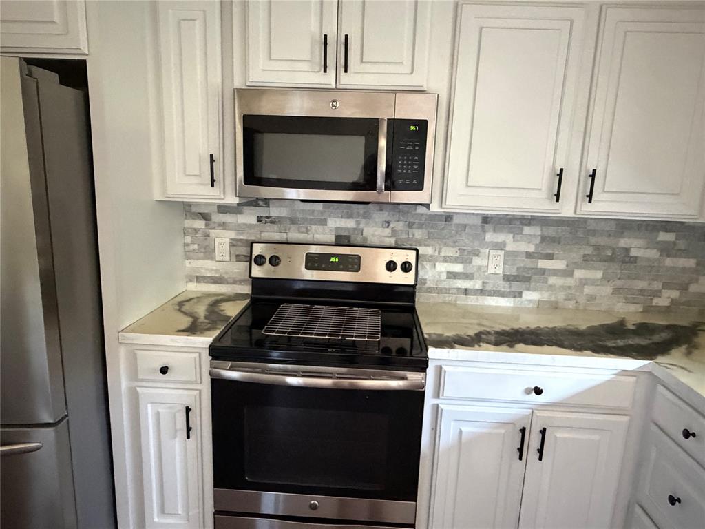 520 Big Red Circle Haughton, LA 71037 - Photo 9 of 25 Kitchen featuring white shaker-style cabinetry with matte black hardware, stainless steel appliances including a range and over-the-range microwave, a patterned tile backsplash, and a unique marbled countertop