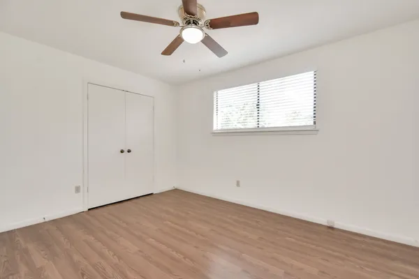an empty room with wooden floor ceiling fan and windows