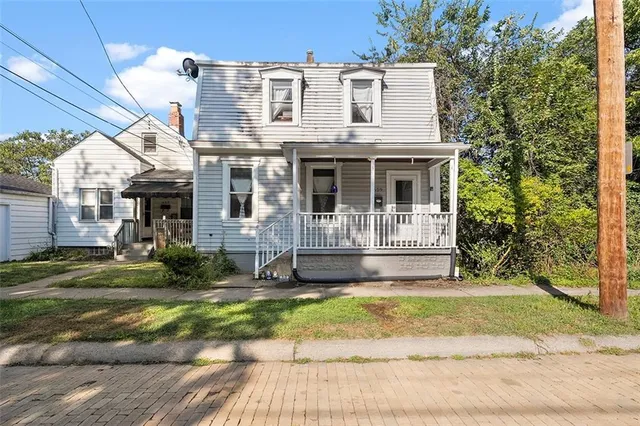 a view of a white house with a small yard plants and large tree