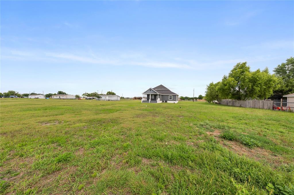 1128 Newton Road Ferris, TX 75125 - Photo 26 of 28 Expansive grassy lot with a detached residence featuring a covered front porch and a dark shingle roof