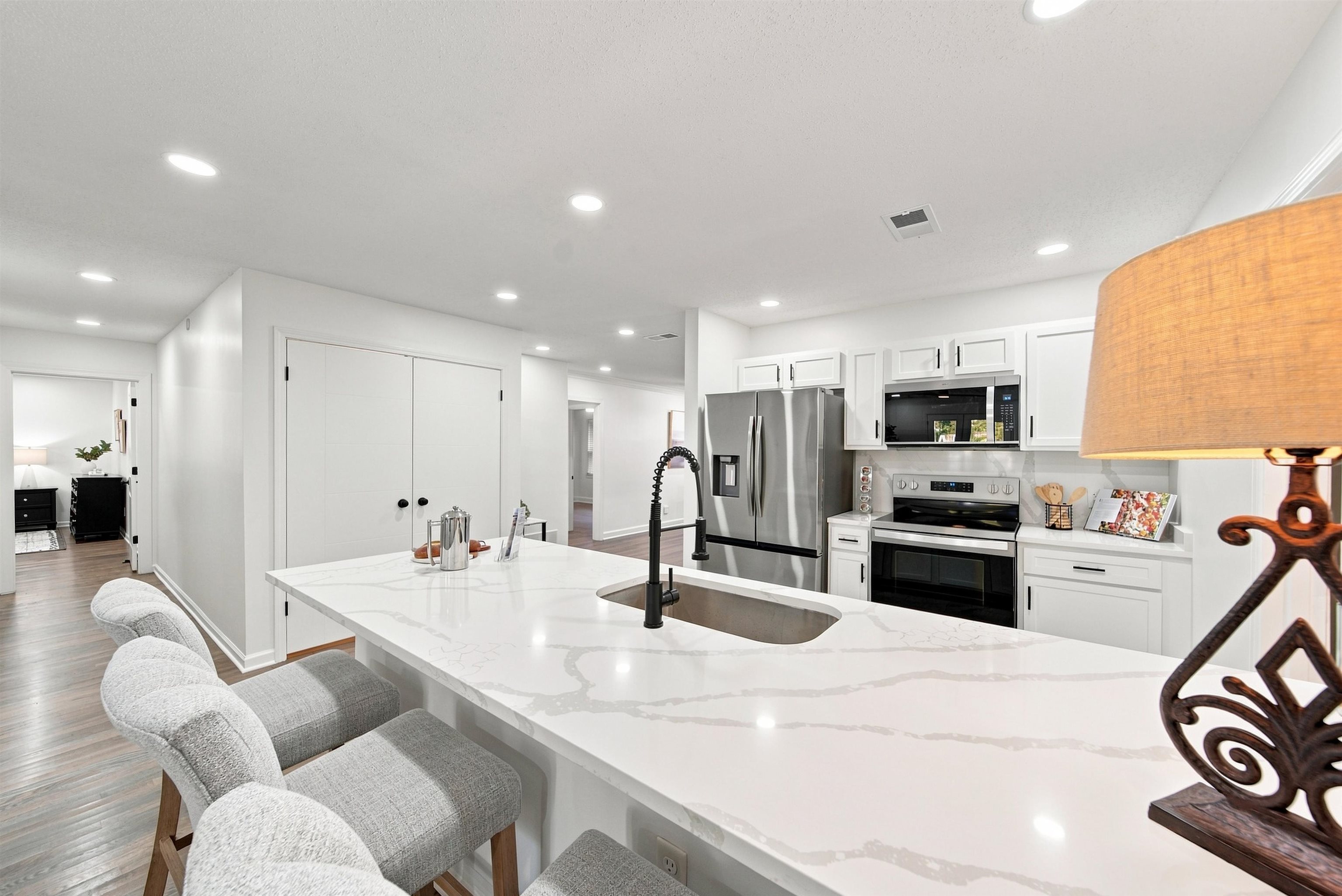 458 Gerald Road Memphis, TN 38122 - Photo 16 of 37 White kitchen cabinetry, stainless steel appliances, solid surface countertops, recessed lighting, and wood-finish flooring