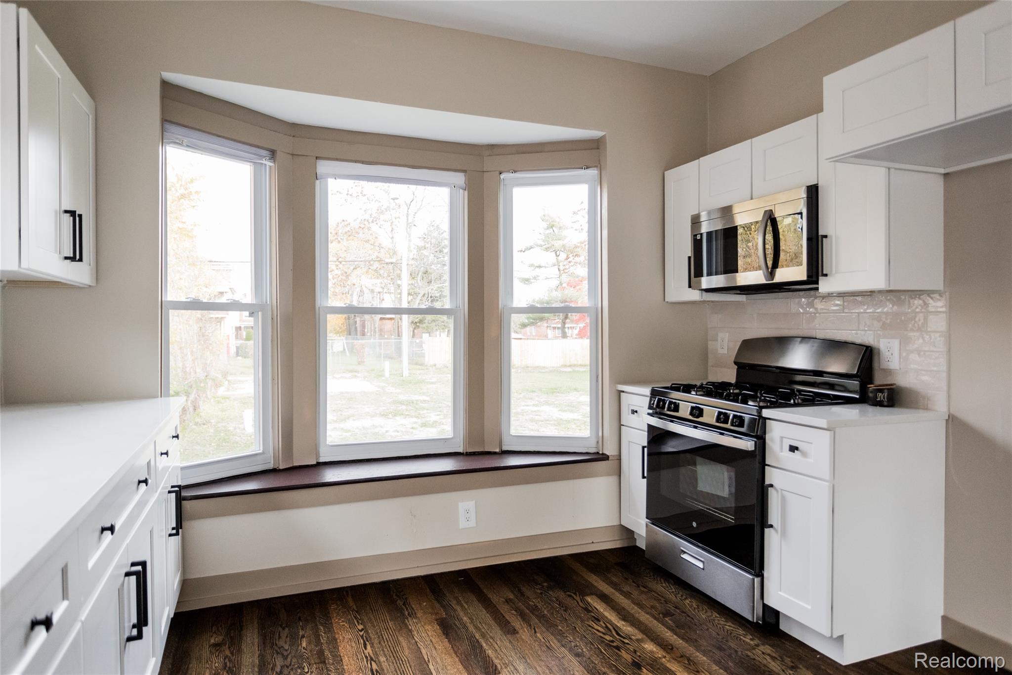 2630 Harding Street Detroit, MI 48214 - Photo 11 of 30 Kitchen featuring a bay window, white shaker cabinetry, stainless steel appliances, white countertops, and wood-finish flooring