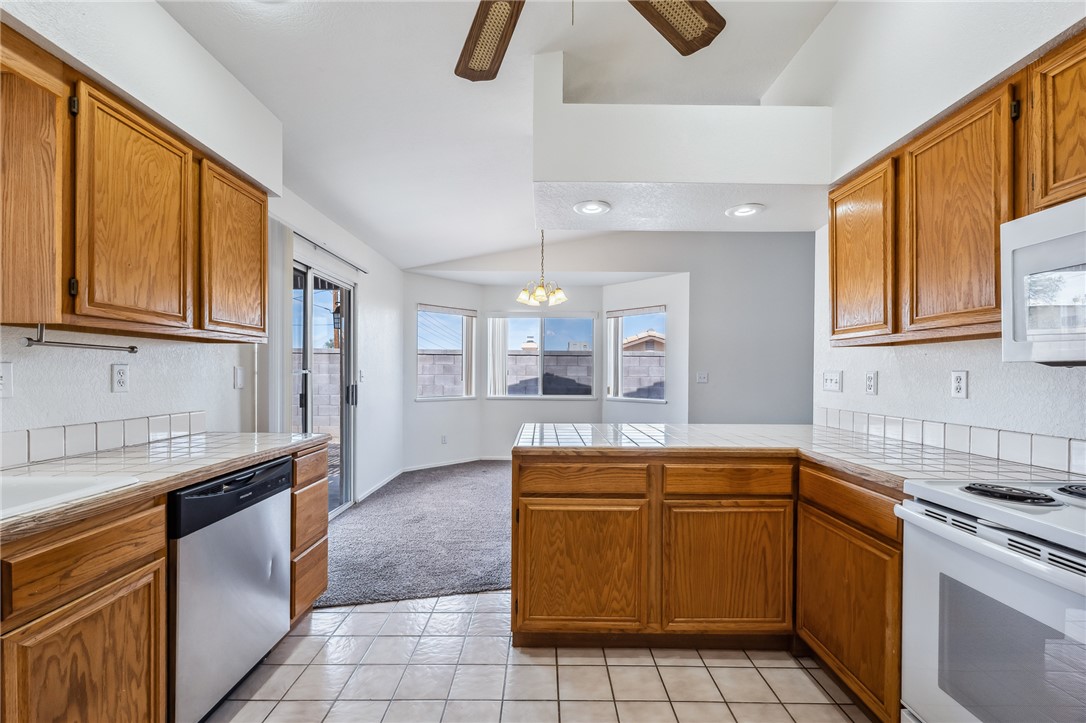 2524 South Ridge Avenue Bullhead City, AZ 86429 - Photo 24 of 64 Kitchen featuring white appliances, lofted ceiling, a peninsula, light tile patterned flooring, and tile counters