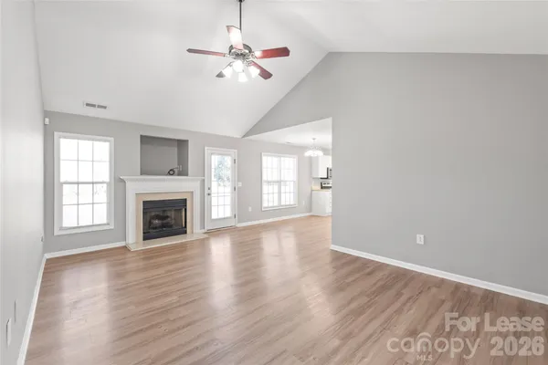 an empty room with wooden floor fireplace and windows