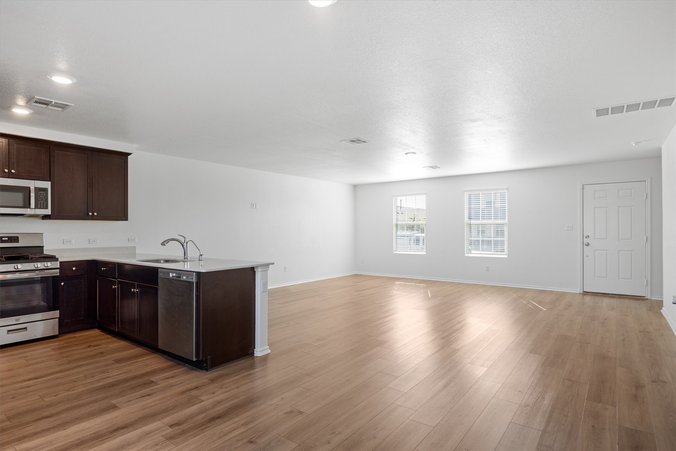 13520 Knights Branch Drive Elgin, TX 78621 - Photo 19 of 20 Kitchen with dark brown cabinetry, appliances with stainless steel finishes, a peninsula, open floor plan, and wood-style vinyl flooring