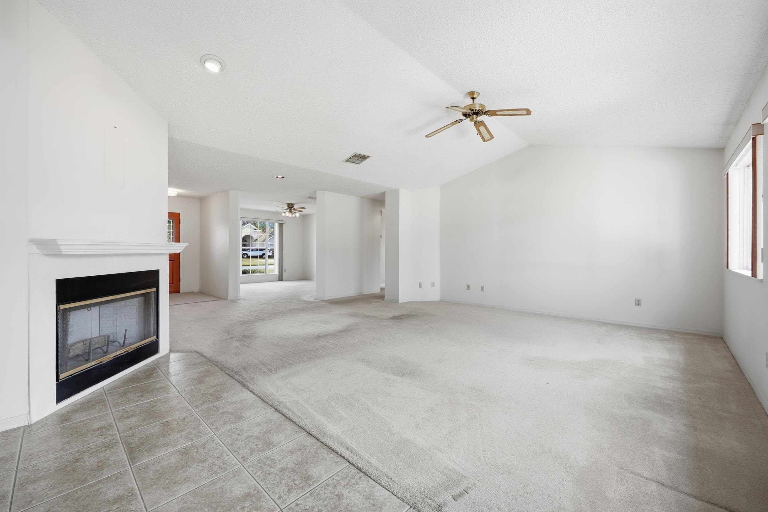 4628 Legends Lane Elkton, FL 32033 - Photo 9 of 49 Unfurnished living room featuring ceiling fan, a glass covered fireplace, lofted ceiling, carpet, and tile patterned flooring