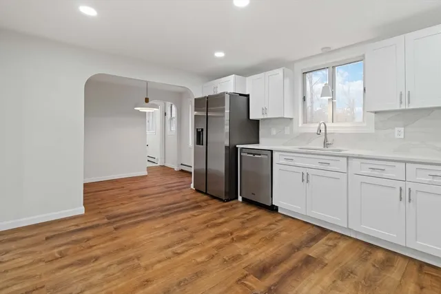 a view of an empty room with wooden floor and a kitchen